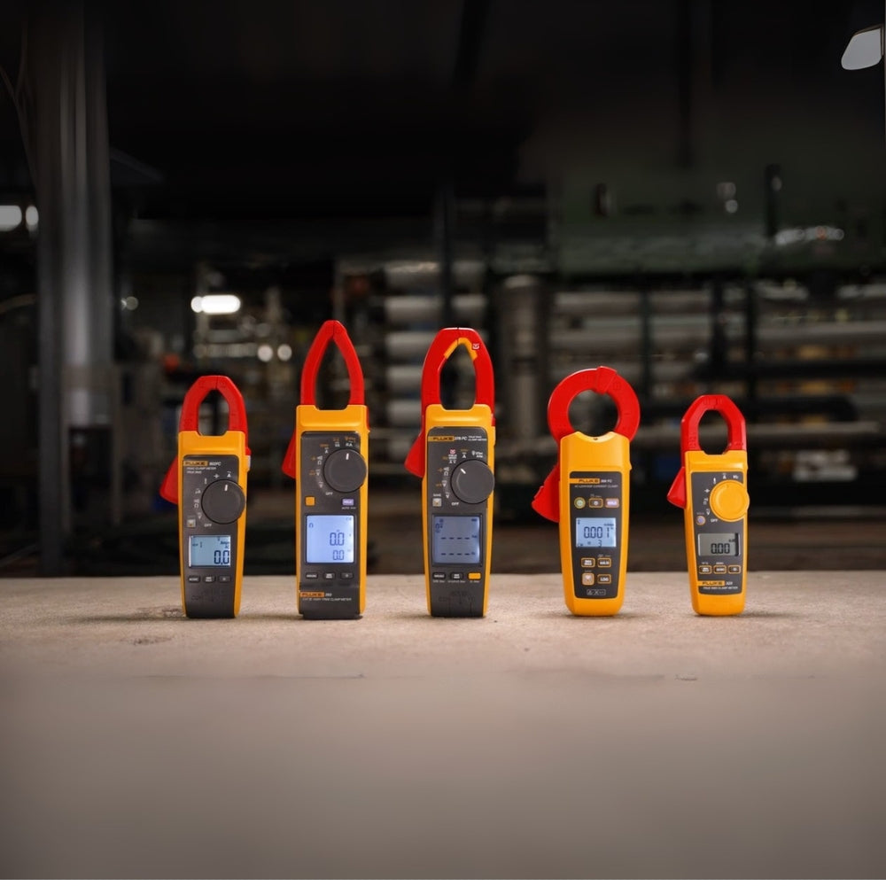 Five digital multimeters with red handles on a concrete floor, blurred industrial background