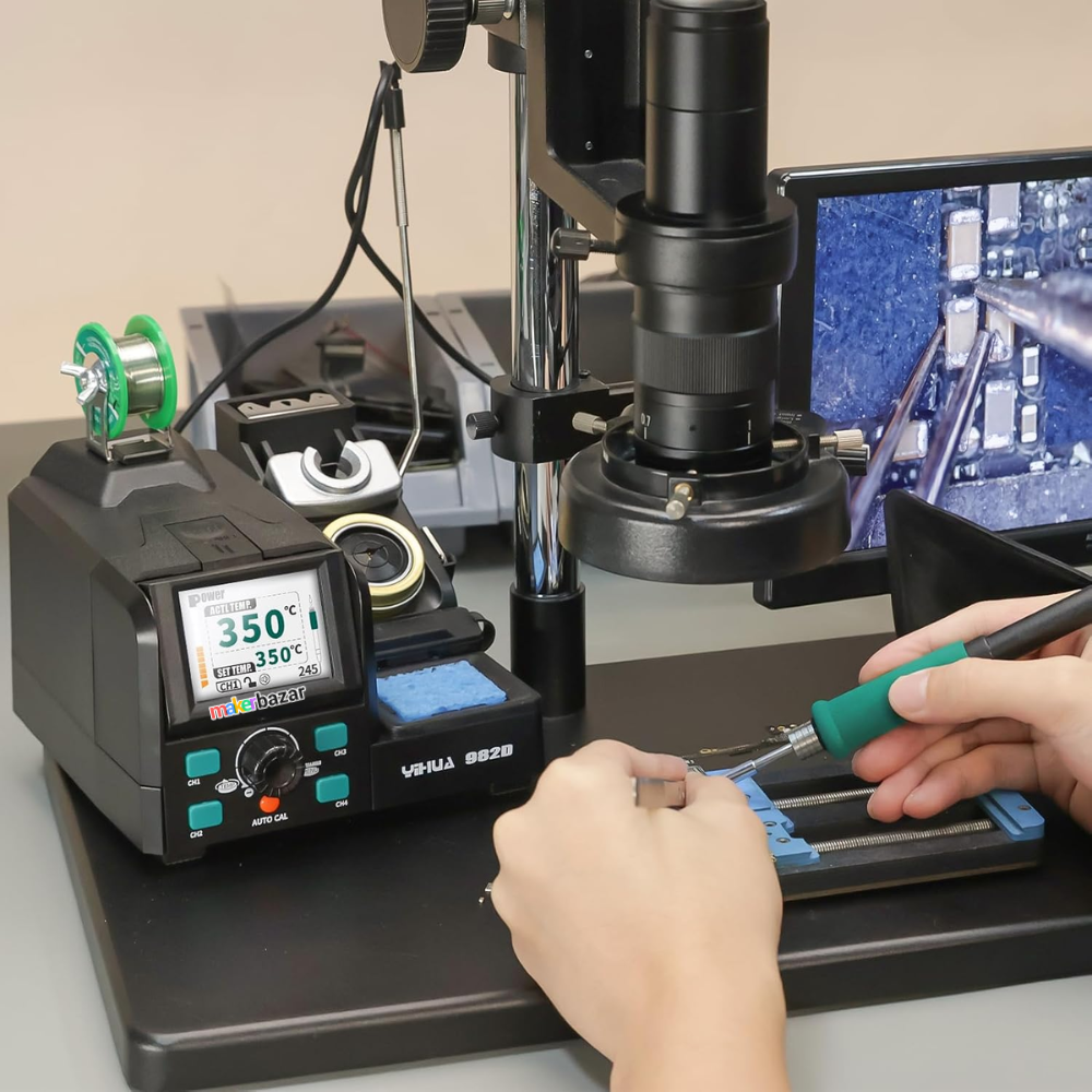 Soldering station with digital display and hands using a soldering iron, with a computer screen in the background.